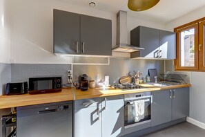 A modern kitchen with grey cabinets, a wooden countertop, a built-in oven, and a window with a view. - La Kaz - Proche de Montluçon (Néris-les-Bains)