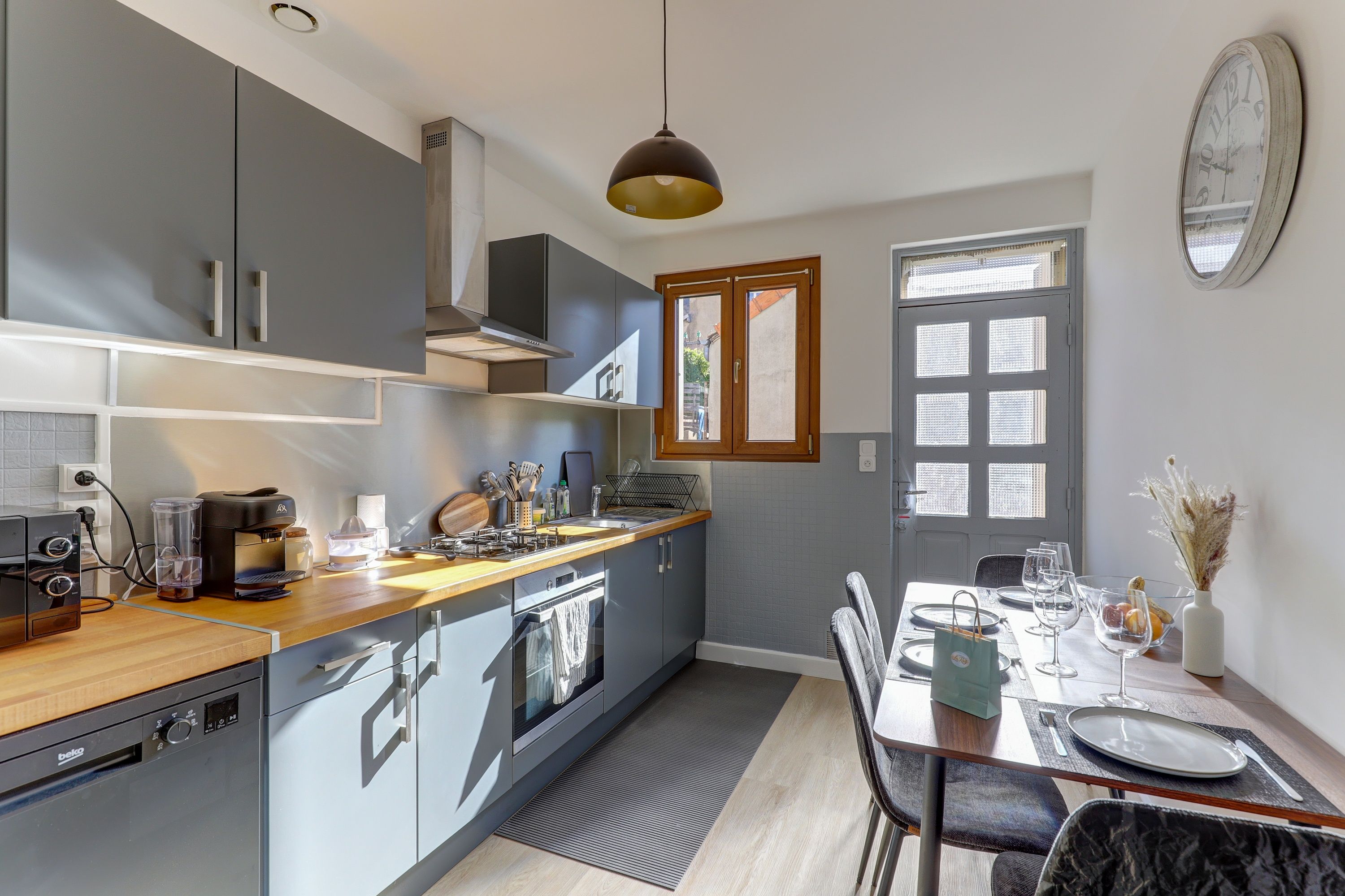 A modern kitchen with a built-in oven, a coffee machine, and a dining area with a table set for two.
