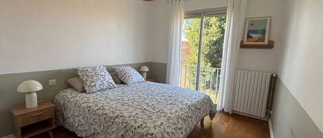 A bedroom with a bed, bedside tables, a hanging light, a window with curtains, and a radiator.
