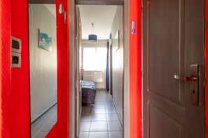 Un corridoio stretto con un letto in fondo, una porta a destra e un lampadario sopra.