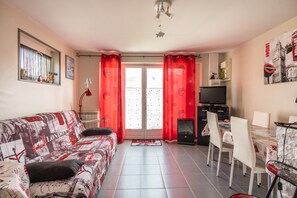 A furnished living room with a sofa, a dining table with chairs, a television, and a radiator. - Clin d’Œil sur la Mer - 300m de la Plage (Cucq)