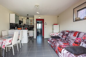 A modern living room with a patterned sofa, a dining area with a table and chairs, and a kitchen with a stove and cabinets. - Clin d’Œil sur la Mer - 300m de la Plage (Cucq)