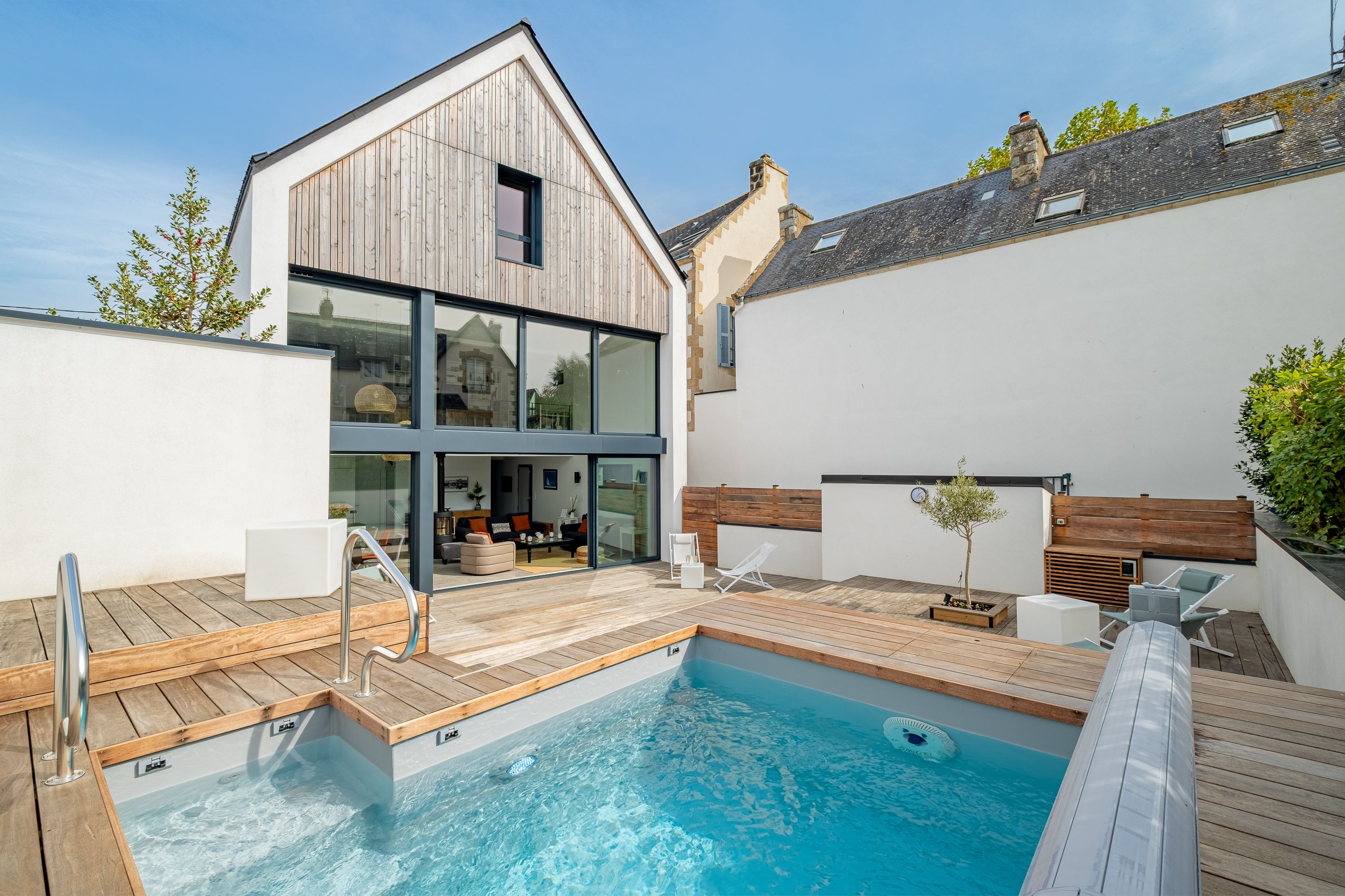 Un espace piscine extérieur moderne, doté d’une terrasse en bois, d’un espace de vie clos par des baies vitrées et d’une piscine à l’eau cristalline.