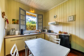 A compact kitchen with a dining area, featuring a sink, stove, and a small refrigerator. - La Case Hoarau Duportail - Case créole du village (Entre-Deux)