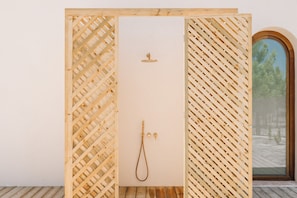 Una habitació de fusta amb dutxa, una porta que ofereix vistes a arbres i un paviment de fusta.