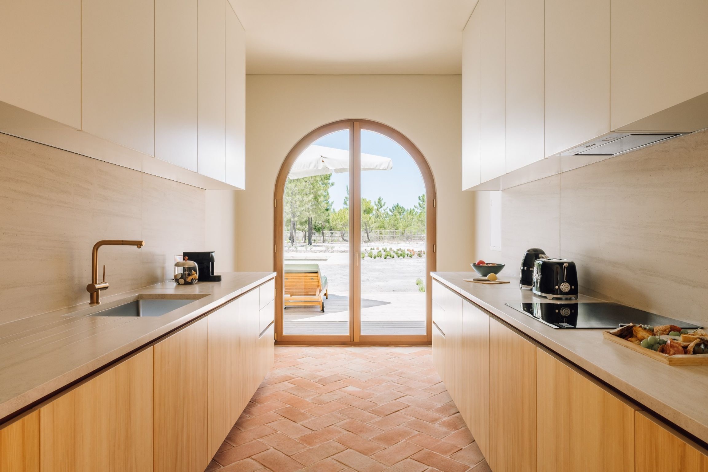 A modern kitchen with a central island, a sink on each side, and a view through an arched doorway to an outdoor seating area.