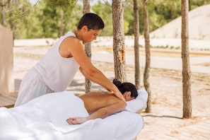 A person receiving a massage outdoors with trees and a building in the background. - Ando Living - Comporta Villas (Grândola)