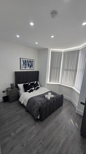 A modern bedroom with a bed, bedside tables, a window with blinds, and a ceiling light. - Spacious 6-Bedrooms all En-suite House Stafford (Stafford)