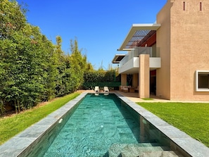 Ein modernes Haus mit Swimmingpool, einer Terrasse und Gartenmöbeln sowie einem gepflegten Garten.