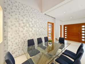 A modern meeting room with a glass table and six chairs, a textured wall, and a wooden door. - Villa avec piscine au prestigieux Noria Golf (Marrakech)