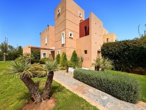 A multi-story building with a modern architectural design, featuring a central courtyard with palm trees and a well-maintained hedge. - Villa avec piscine au prestigieux Noria Golf (Marrakech)