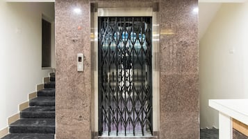 Un ascensor con una puerta metálica, una escalera a la izquierda y una pared lisa.