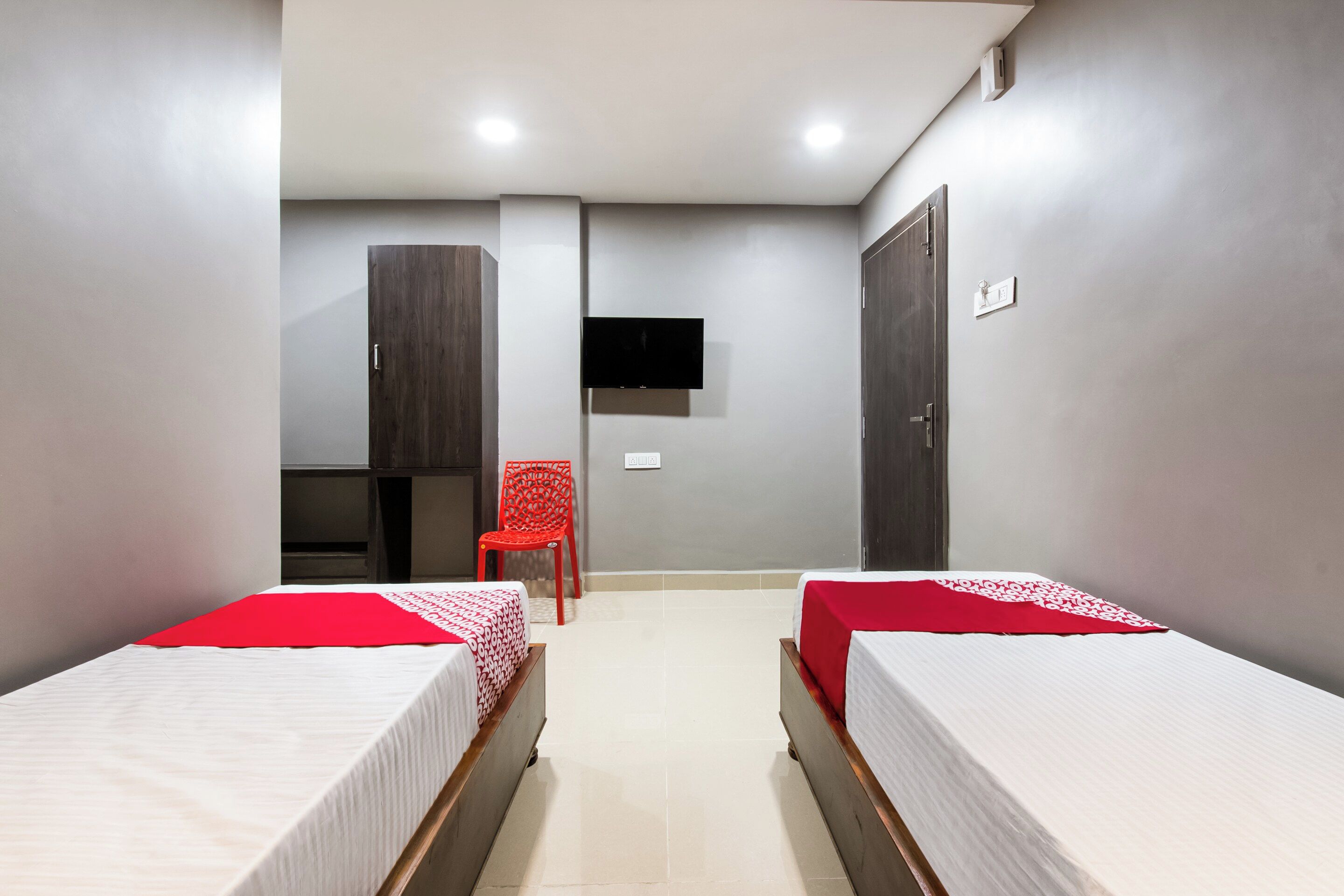 Habitación de hotel con dos camas, un televisor, una silla roja y un armario.
