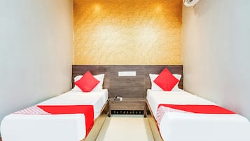 A hotel room with two single beds, a wooden headboard, a wall-mounted air conditioner, and a small bedside table with a phone.