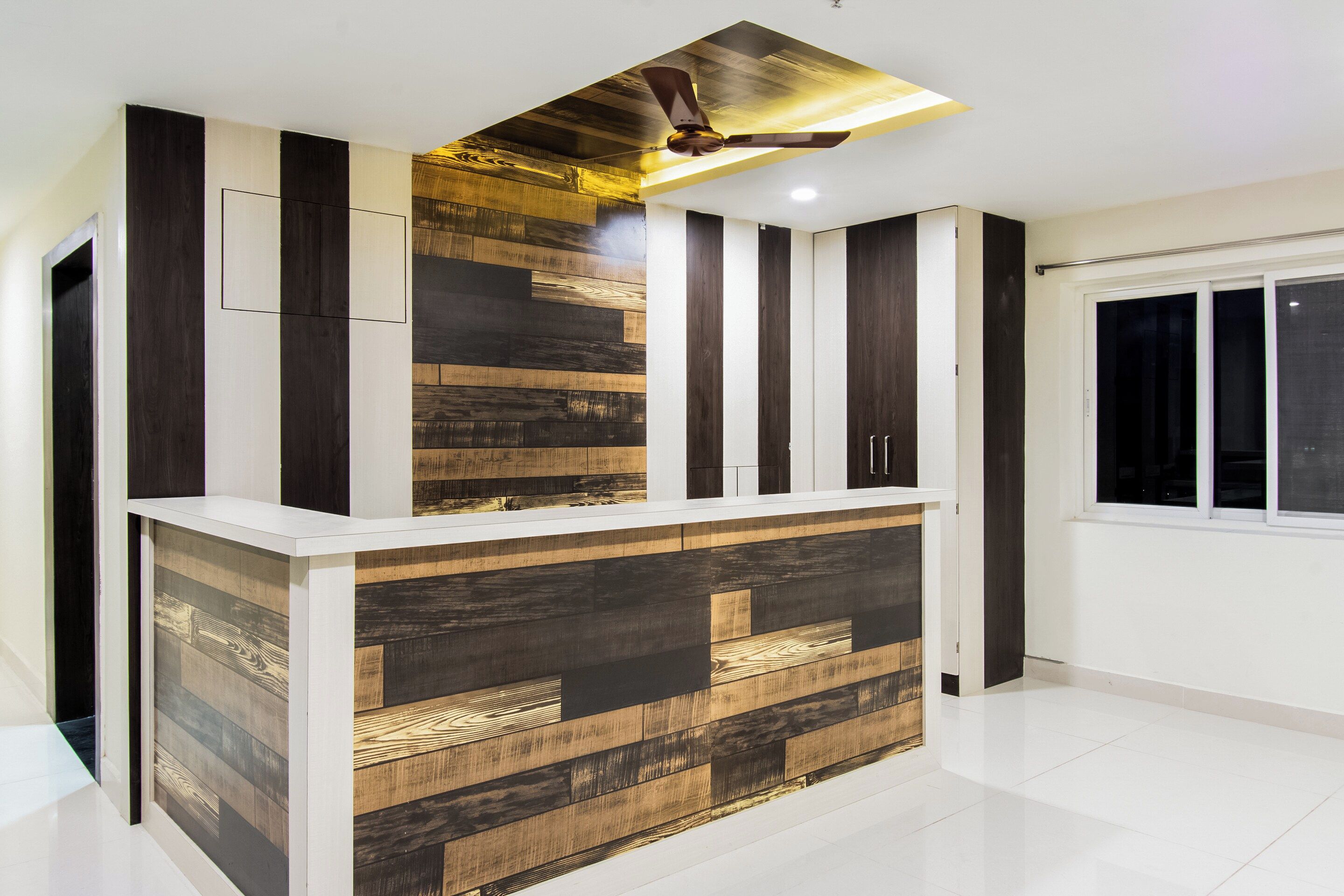 A modern reception desk with a wooden panel design, a ceiling fan, and a window with a view.