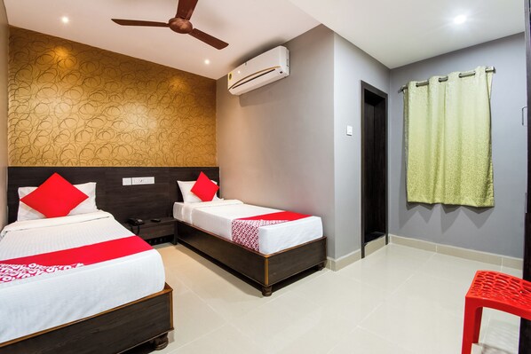 A hotel room with two beds, a ceiling fan, an air conditioning unit, a patterned wall, a door, and a red chair. - Hotel O CJ Inn (Vijayawada)