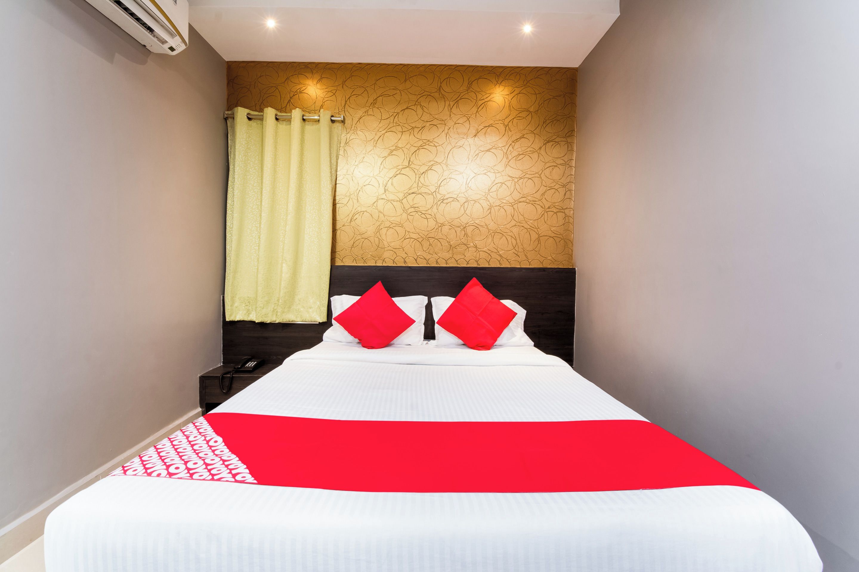 A hotel room with a bed, a nightstand, a telephone, and a wall-mounted air conditioning unit.