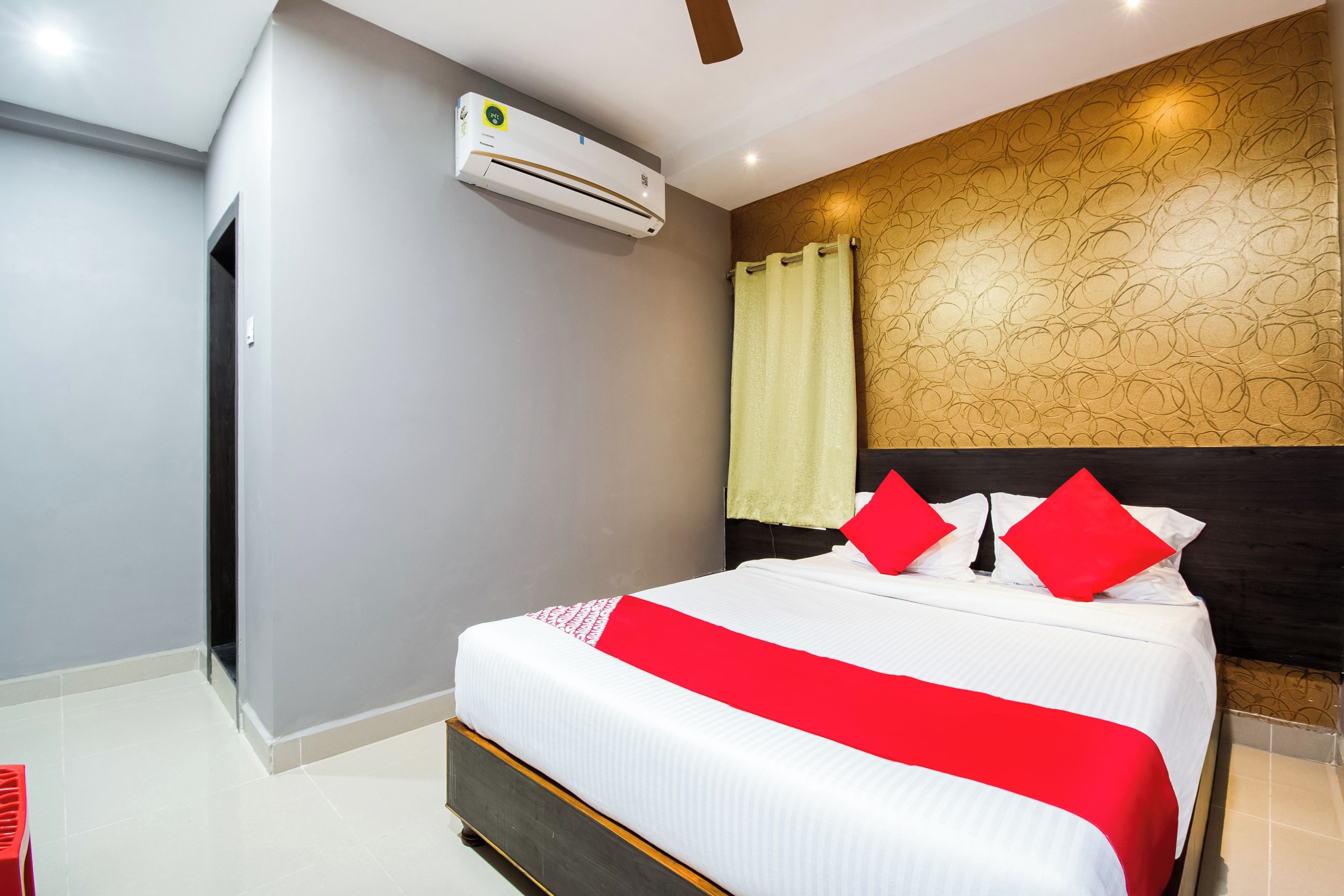 Ein Hotelzimmer mit einem Bett, einem Deckenventilator, einer Klimaanlage, einer Wand mit Muster und einem Vorhang.