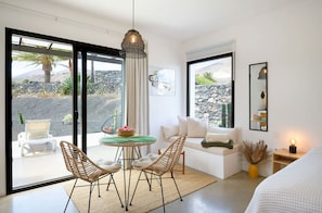 A modern room with a glass door leading to an outdoor area, a round table with chairs, a sofa, and a bed. - Fantastic 3-bedroom house with heated pool in Tías perfect for your getaway (Tías)