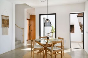 Et moderne spiseområde med et glasbord, fletstole og en hængende pendellampe.