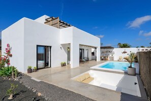 Ein modernes Haus mit Swimmingpool, Sitzgelegenheit im Freien und blauem Himmel.