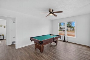 A pool table in a room with a ceiling fan, large windows, and a view of the outside. - Vibrant 3BR Home, Blue Kitchen & Game Room (Abilene)