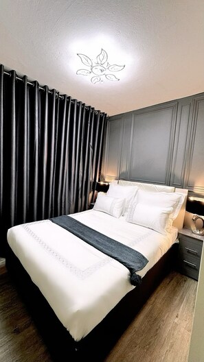 A neatly made bed with white linens and a gray throw, a bedside table with a lamp, and a dark curtain covering a window. - Fantastic 2-bedroom apartment with AC in vibrant Sandton (Sandton)
