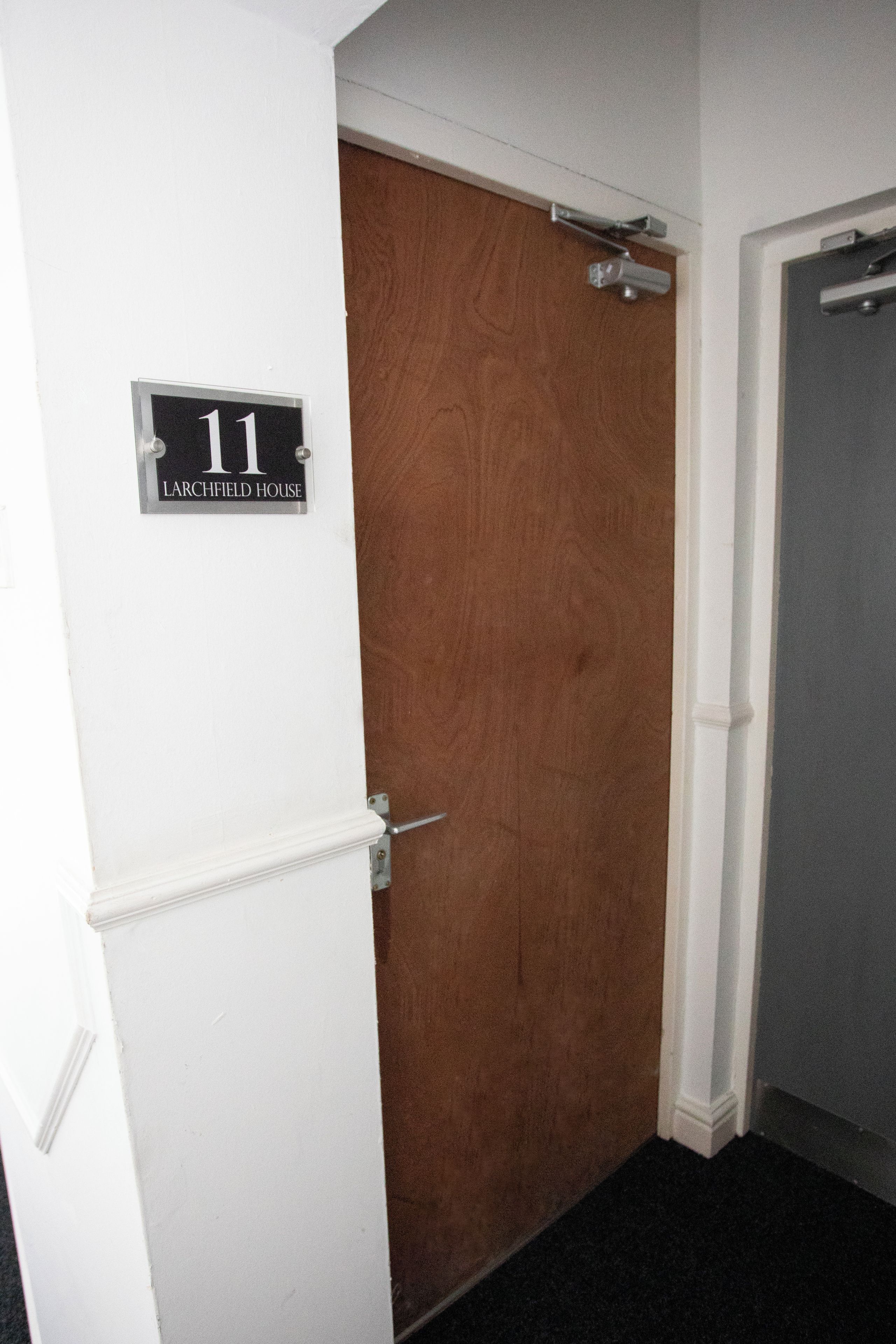 Un pasillo con una puerta de madera marcada con el número 11 y una puerta blanca.