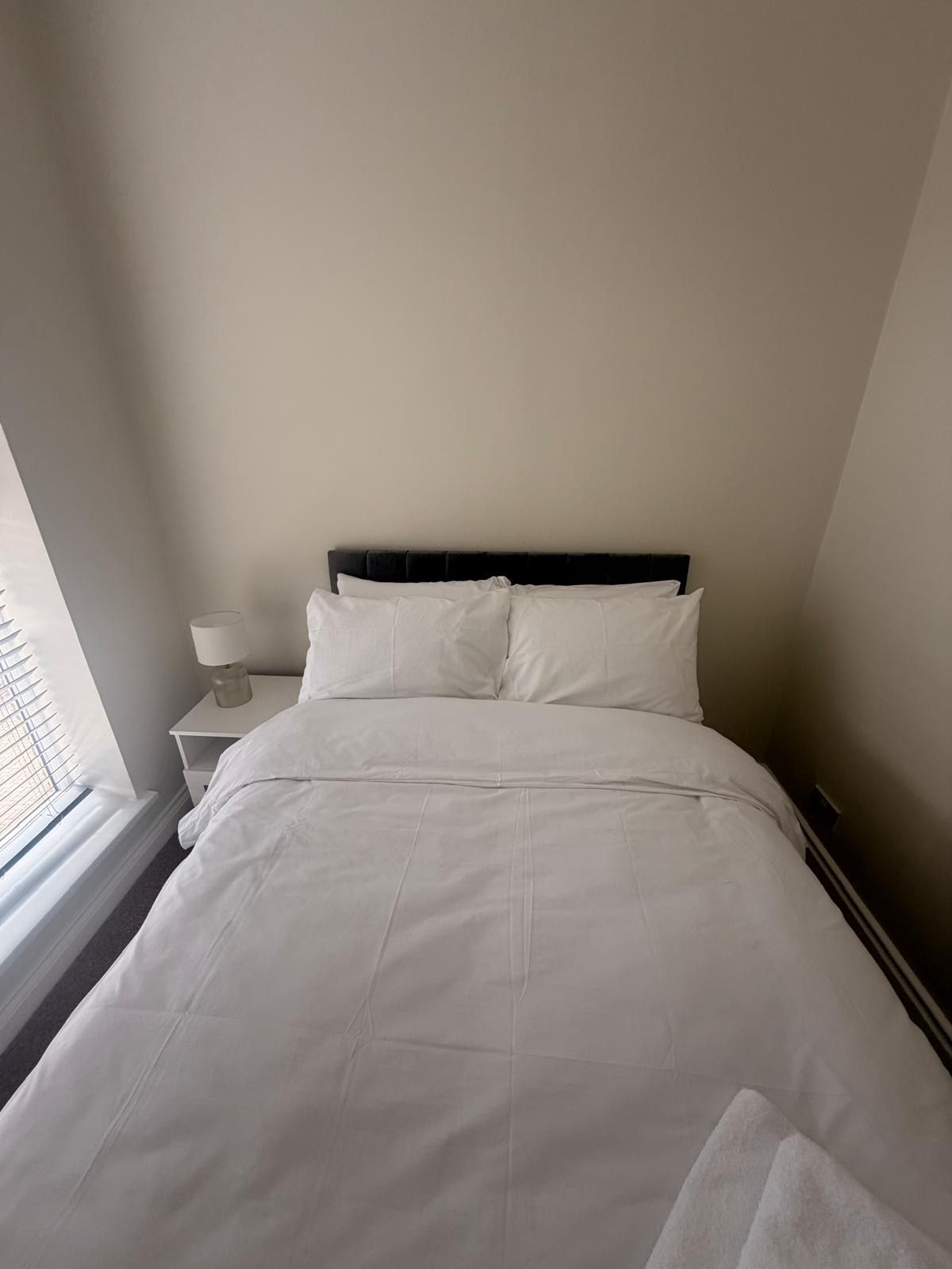 Una cama bien tendida con sábanas blancas en una habitación de diseño sencillo y limpio.