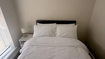 Una cama bien tendida con sábanas blancas en una habitación de diseño sencillo y limpio.