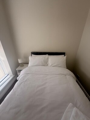 A neatly made bed with white linens in a room with a simple, clean design. - 11 Larchfield House  (Darlington)