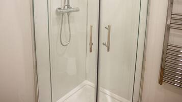 Un box de ducha con paredes de vidrio, cabezal de ducha de mano y grifo empotrado.