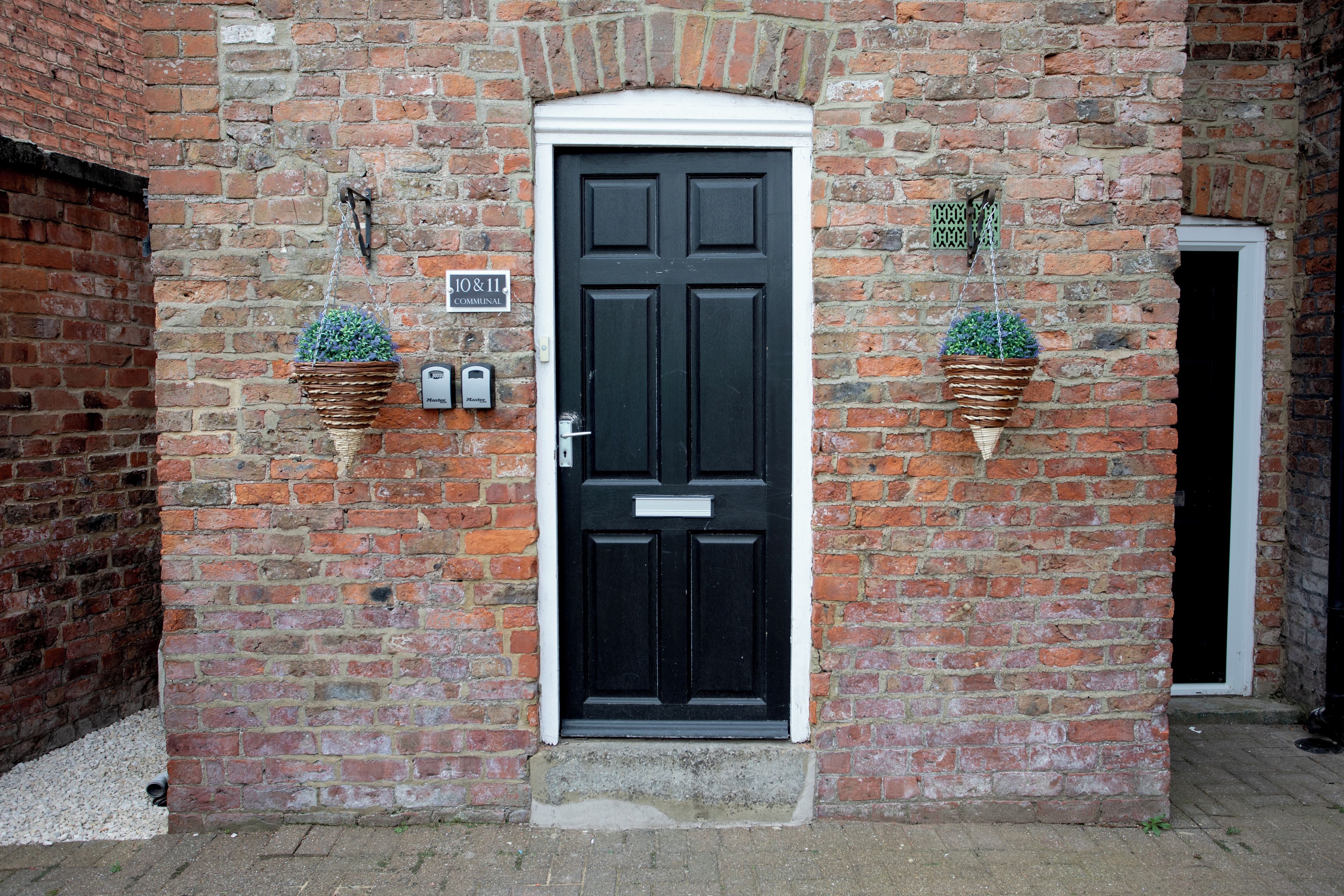 A black door with a white frame, flanked by two hanging flower baskets.