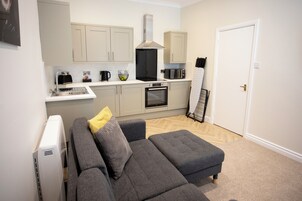 A compact living space with a kitchenette, grey sofa, and a door leading to another room.