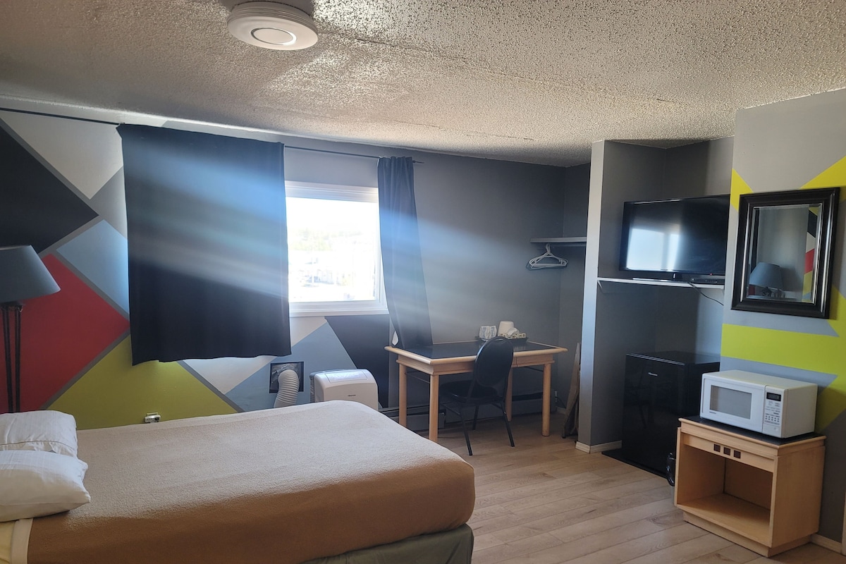 Una habitación de hotel con cama, escritorio, silla, televisor y microondas.