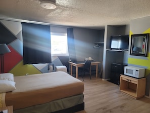 Una habitación de hotel con cama, escritorio, silla, televisor y microondas.