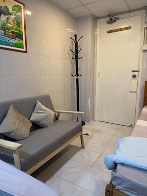 Una habitación con un sofá gris, un perchero, una cama y una puerta con pomo.