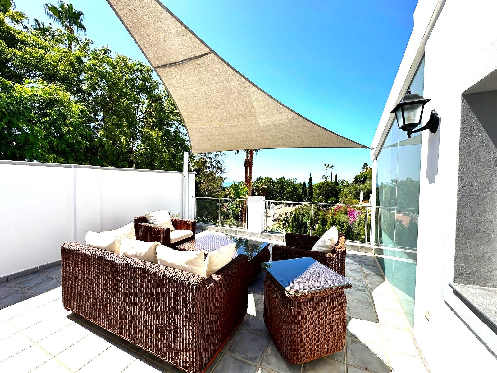 An outdoor patio with wicker furniture, a glass table, and a large canopy.