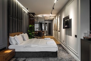 Ein modernes Hotelzimmer mit einem großen Bett, einem Schreibtisch, einem Sessel, einem Fernseher und einem großen Fenster mit Blick auf die Stadt.