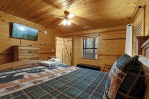A wooden cabin room with a bed, a television, a ceiling fan, and a window. - Family Friendly-Game Room-Hot Tub-Fireplace (Sevierville)