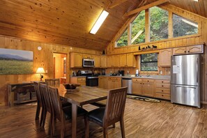 A wooden cabin interior with a dining area, kitchen, and large windows. - Family Friendly-Game Room-Hot Tub-Fireplace (Sevierville)