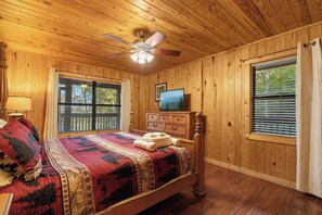 Une chambre aux murs lambrissés, avec un lit, une commode et un ventilateur de plafond.