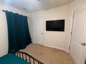 Ein Schlafzimmer mit einem Bett, einer Tür, einem an der Wand befestigten Fernseher und einem Teppichboden.