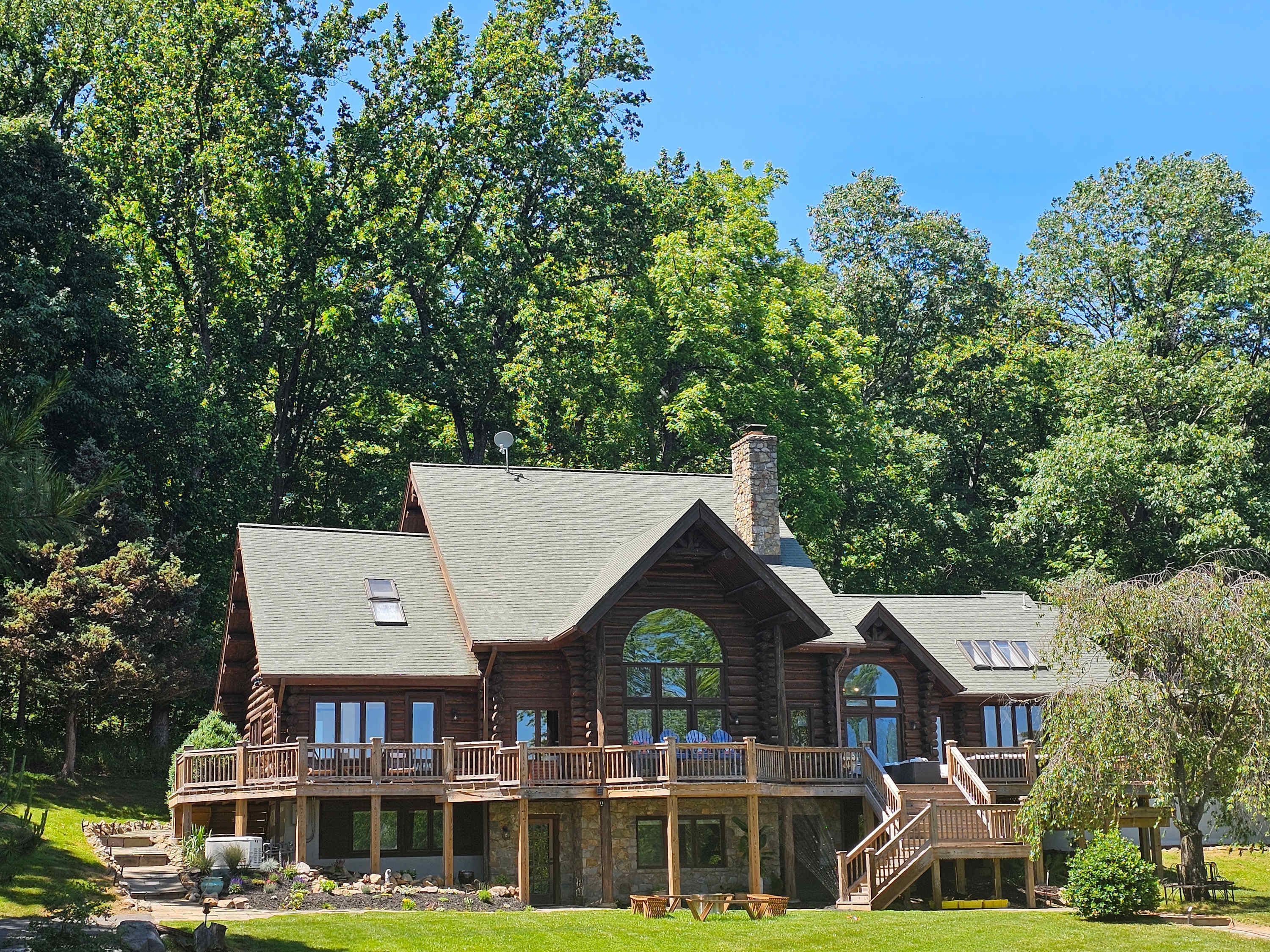 A large log cabin with multiple decks and a stone chimney.