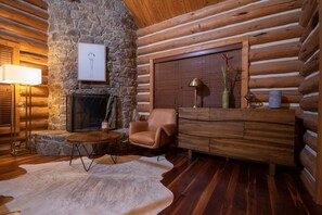 A log cabin interior with a stone fireplace, a leather armchair, a wooden cabinet, and a floor lamp. - Vinewood Estate Luxury Pool and Vineyard Retreat (Purcellville)