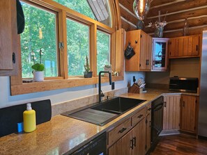 Eine Küche mit Holzausstattung, einer Edelstahl-Spüle und einem Fenster mit Blick auf einen Wald.
