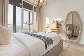 A modern bedroom with a large bed, a bedside table, a mirror, and a view of the city. - Stylish High-Floor 1BR w/ Open Skyline Views, Minutes on Foot from Circle Mall (Dubai)