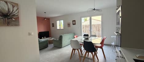 A modern living space with a dining area, a sofa, a TV, and a kitchen area with appliances.