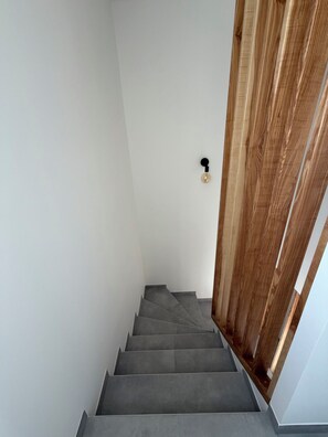 A staircase with grey steps leading upwards, a wooden door frame, and a light switch on the wall. - La Villa d'Anna, located in Peynier (a 6-sleeper home) (Peynier)