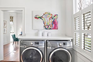 A laundry area with two front-loading washing machines, a white countertop, and a colorful cow painting above them. - Wilson Place (Mobile)